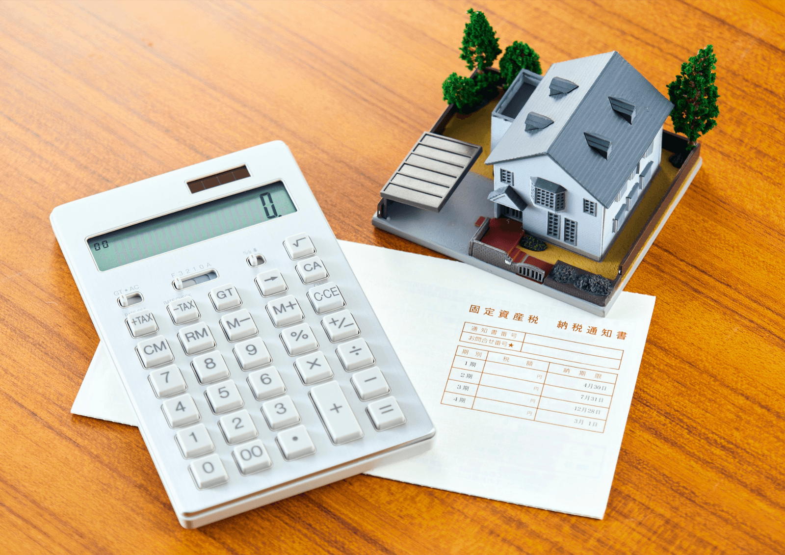 Calculator and a miniature house model resting on a tax document on a wooden desk.