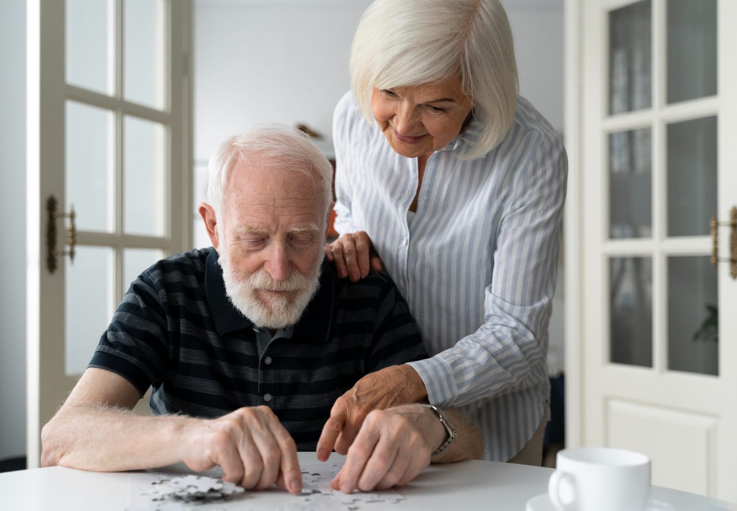 An older man and woman collaborate on a jigsaw puzzle, focused and engaged in the activity together.