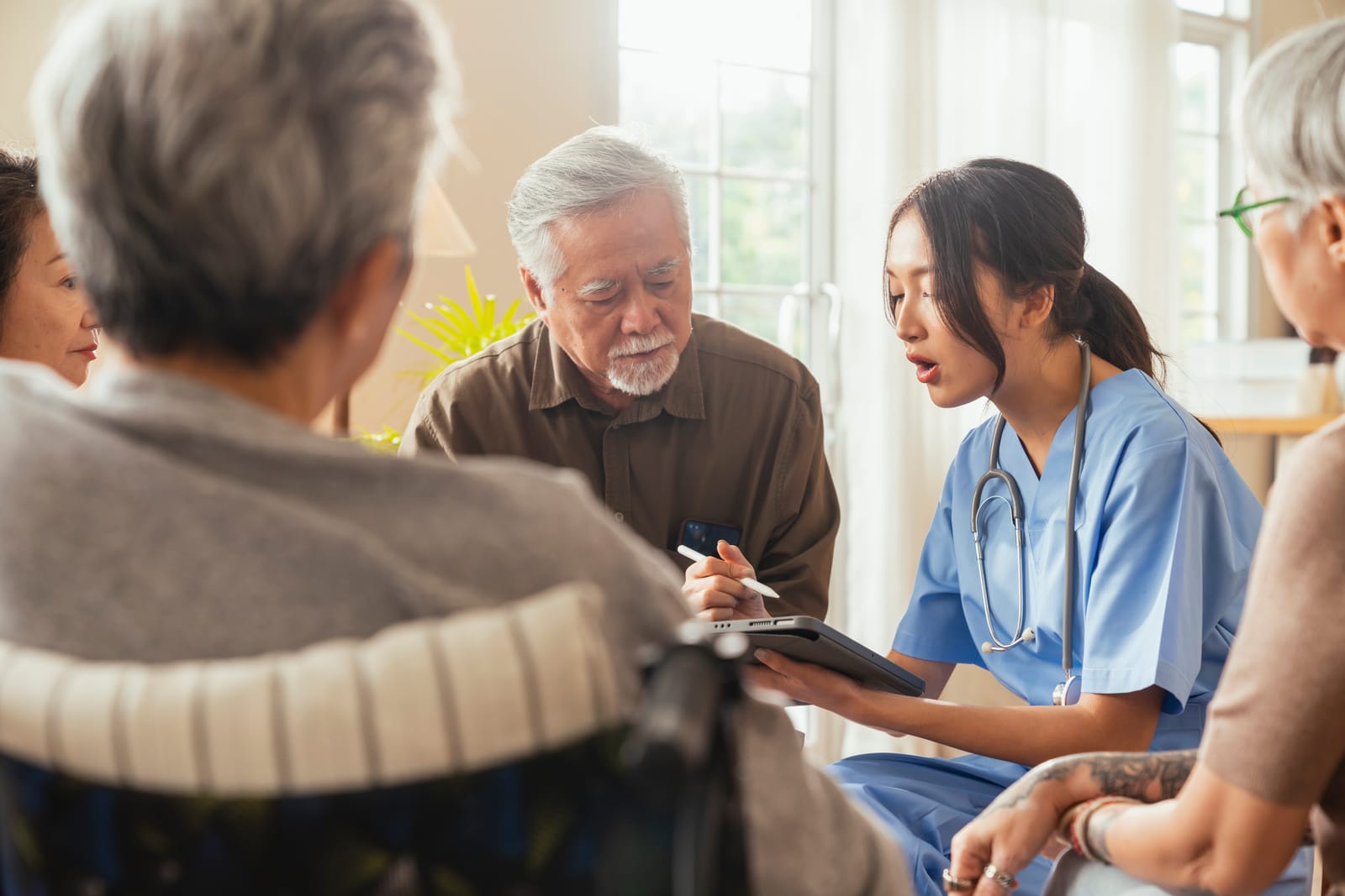 Happiness cheerful elderly woman and men talking with female caregiver nurse doctor having health checking consult at living areacaretakers with senior couple sitting in living room at nursing home