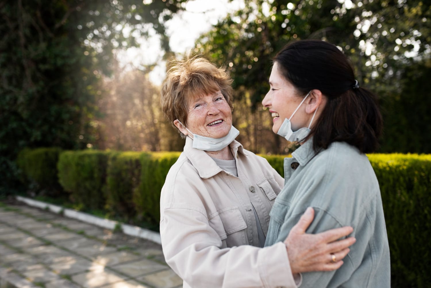 An older woman with short brown hair and a younger woman with dark hair embrace outdoors.