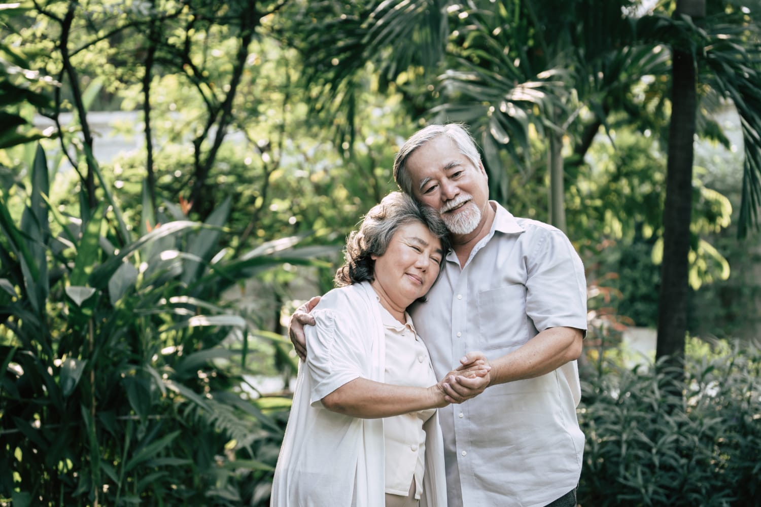 An older couple sharing a warm embrace in a lush garden filled with flowers.