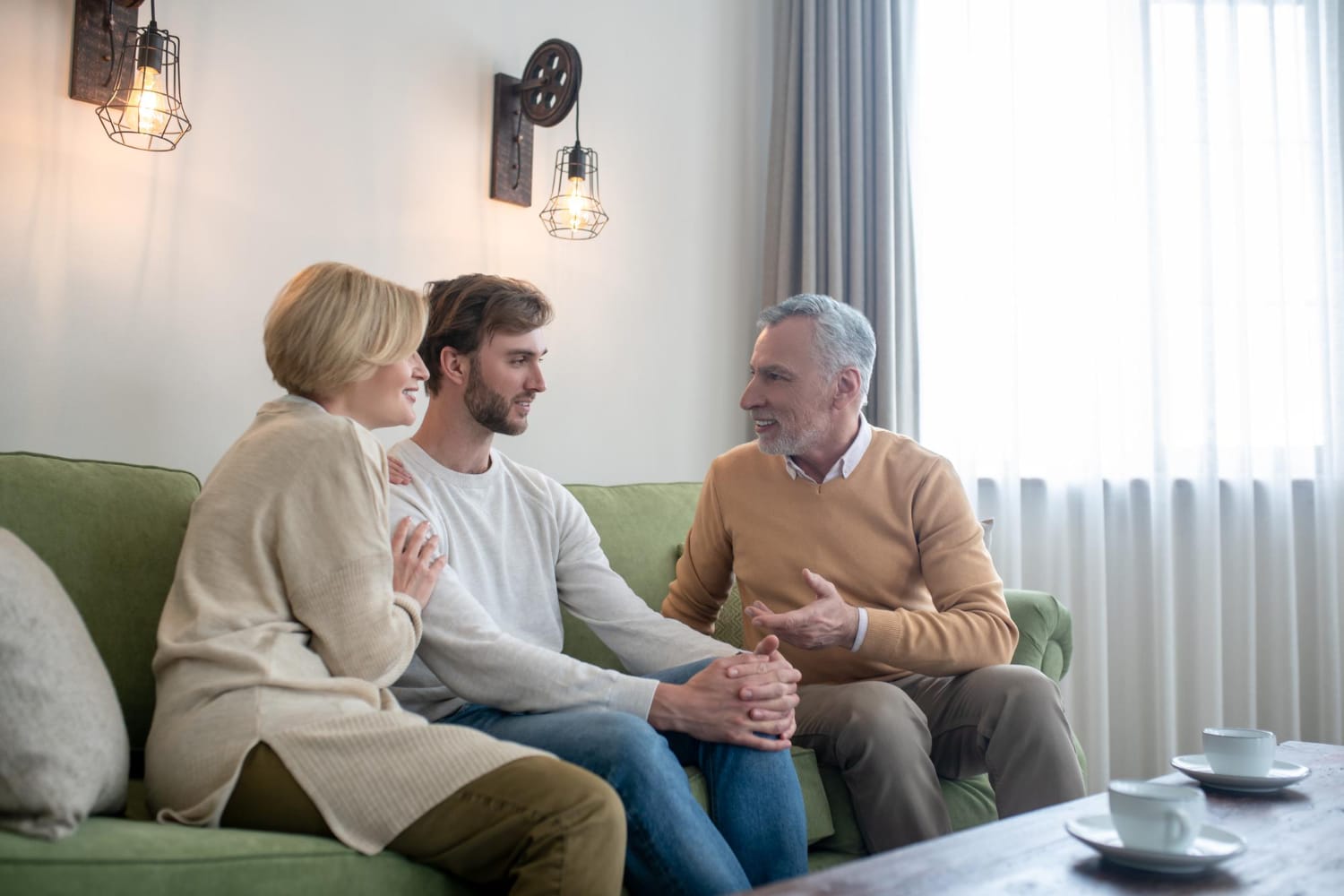 Three people sit on a green couch having a conversation. 