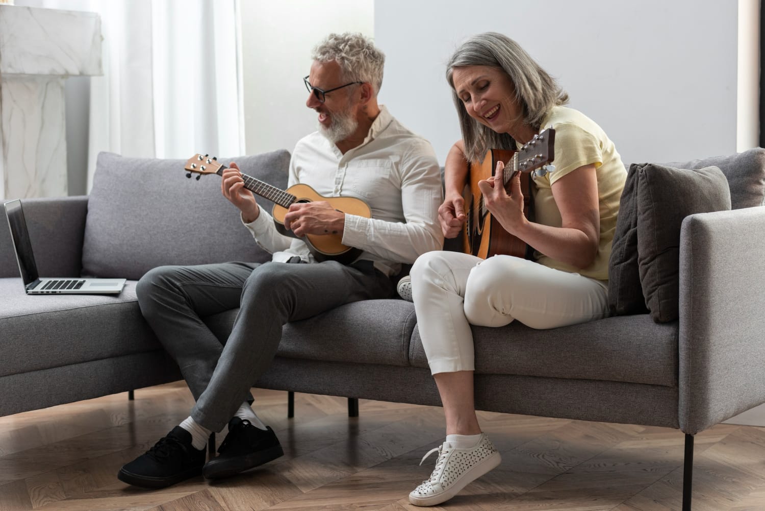 Senior couple at home studying guitar and ukulele lessons on laptop