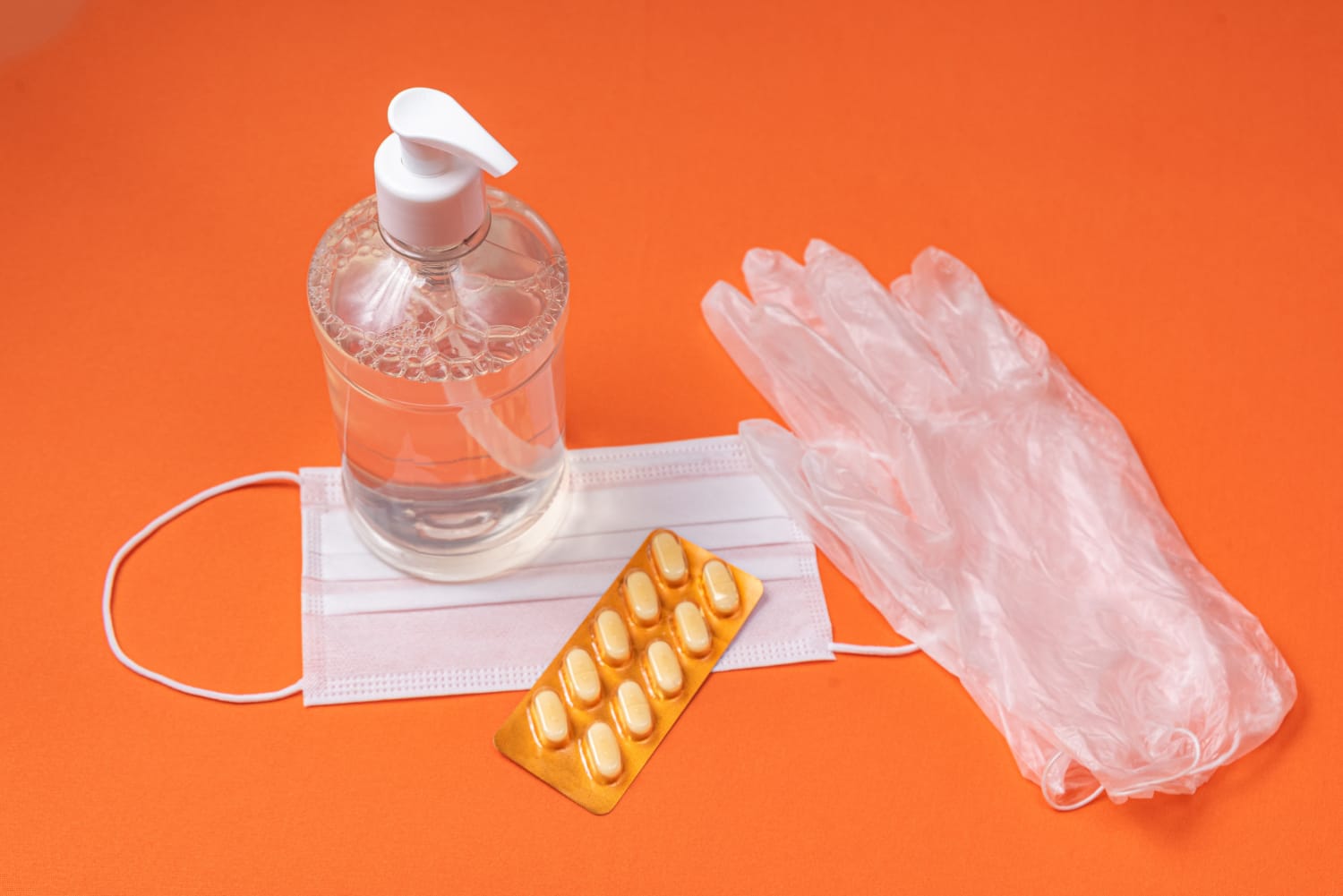 Container with alcohol gel, gloves and surgical mask on the orange wall