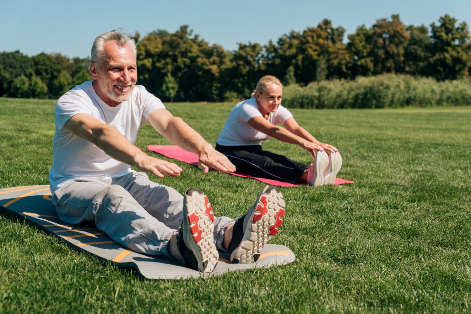Senior couple practicing stretching exercises together in a sunny park, promoting health and wellness.