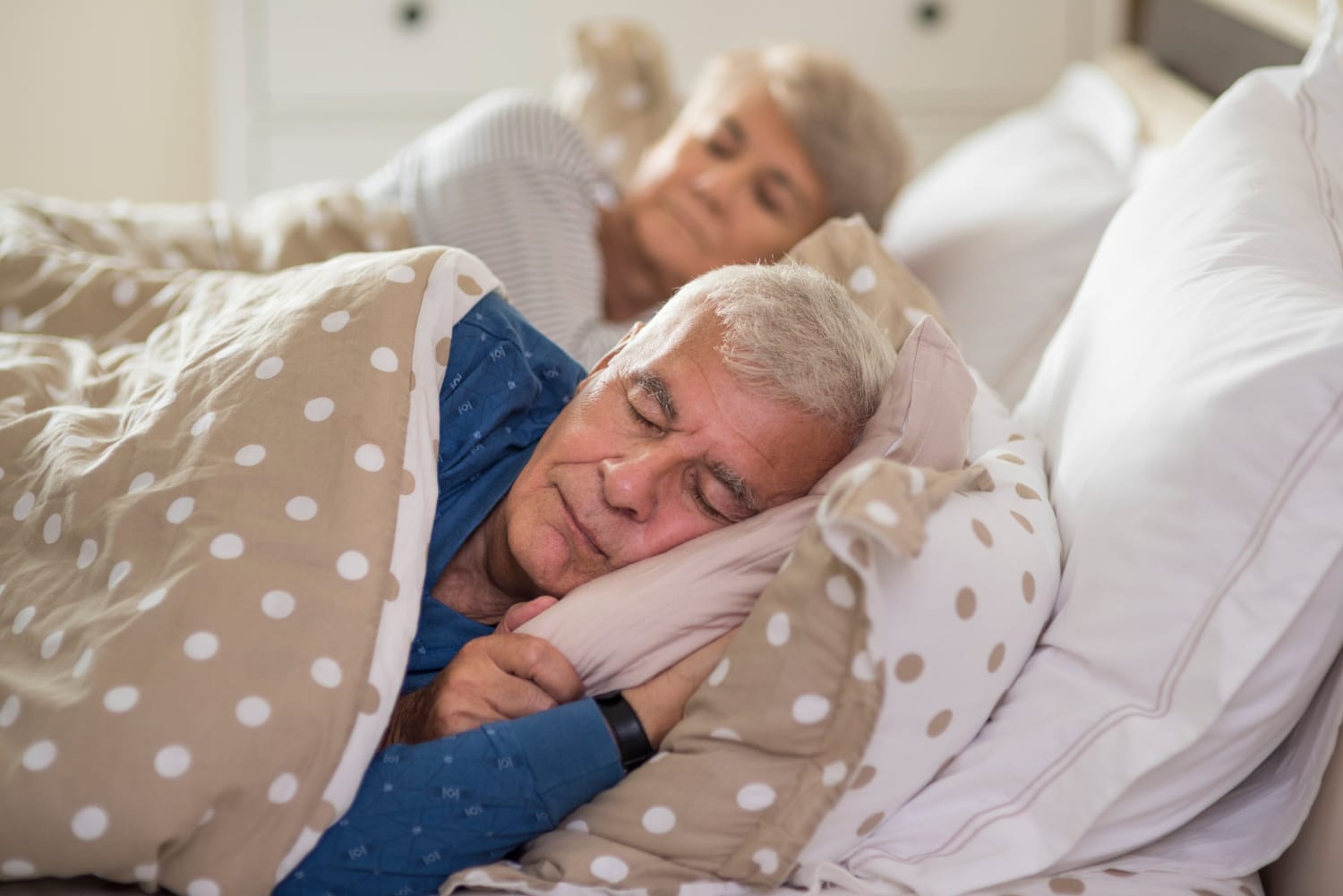 An older man and woman peacefully sleeping together in a cozy bed.