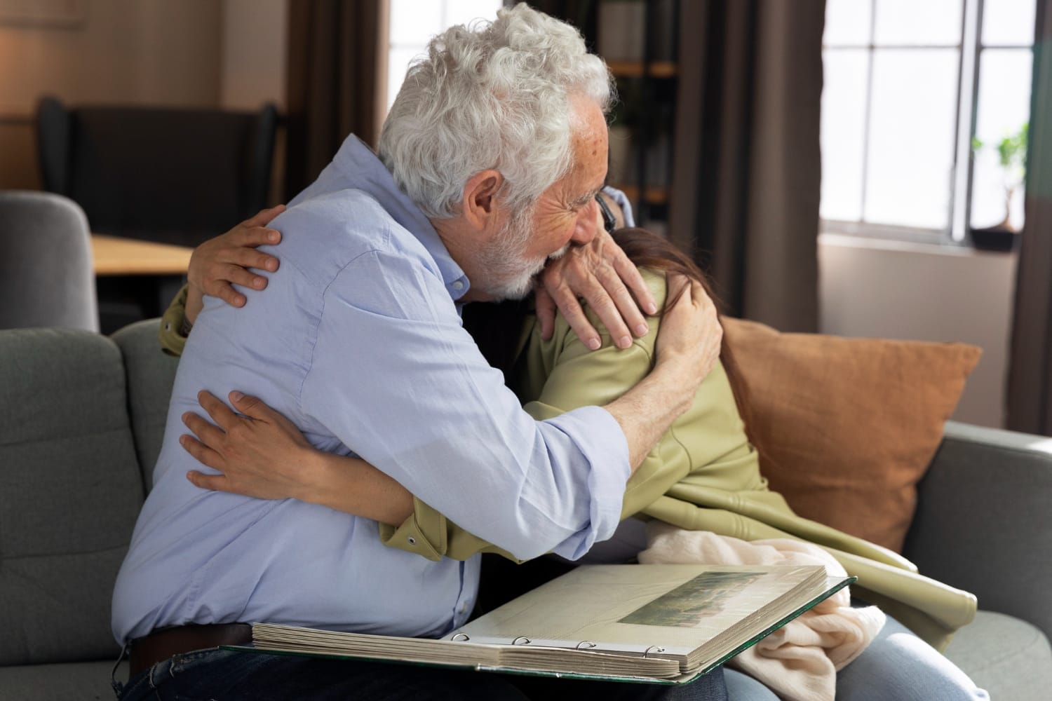 An older man and woman embrace affectionately while sitting together on a couch.