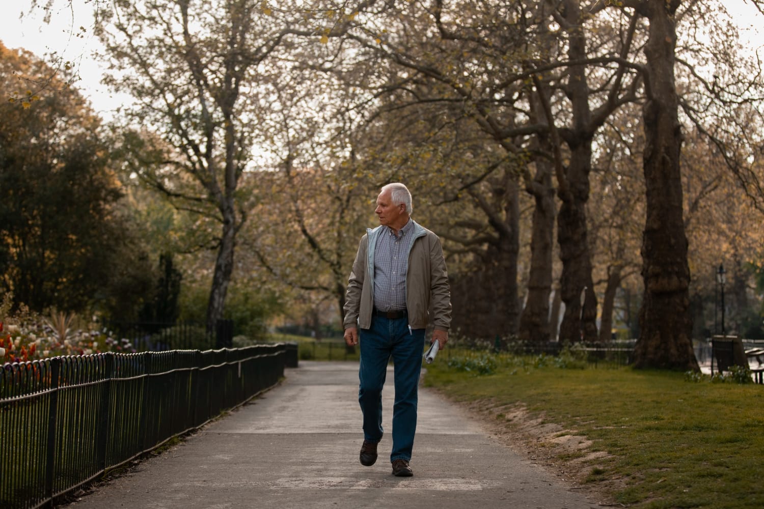 An older man walking along a tree-lined path in a park, enjoying the outdoors.