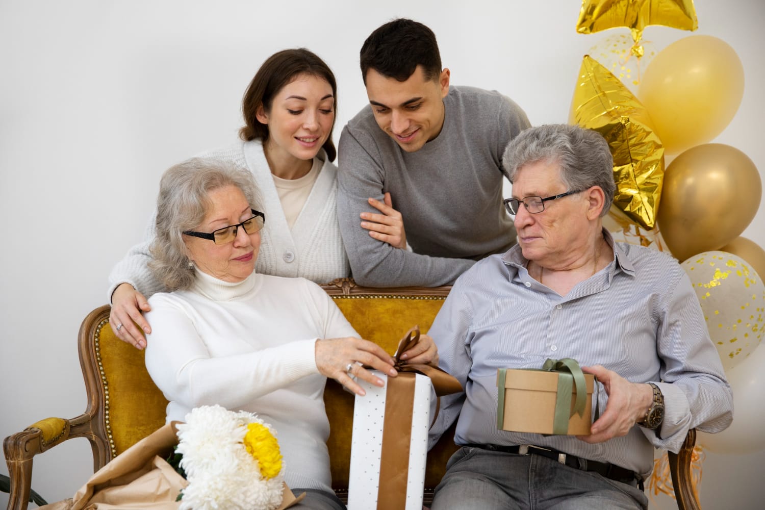 A family of four sits on a couch, smiling at a colorful gift box placed in front of them.