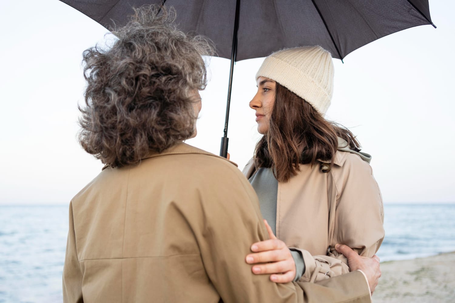 Mother and daughter sharing a tender moment while on the beach under an umbrella.