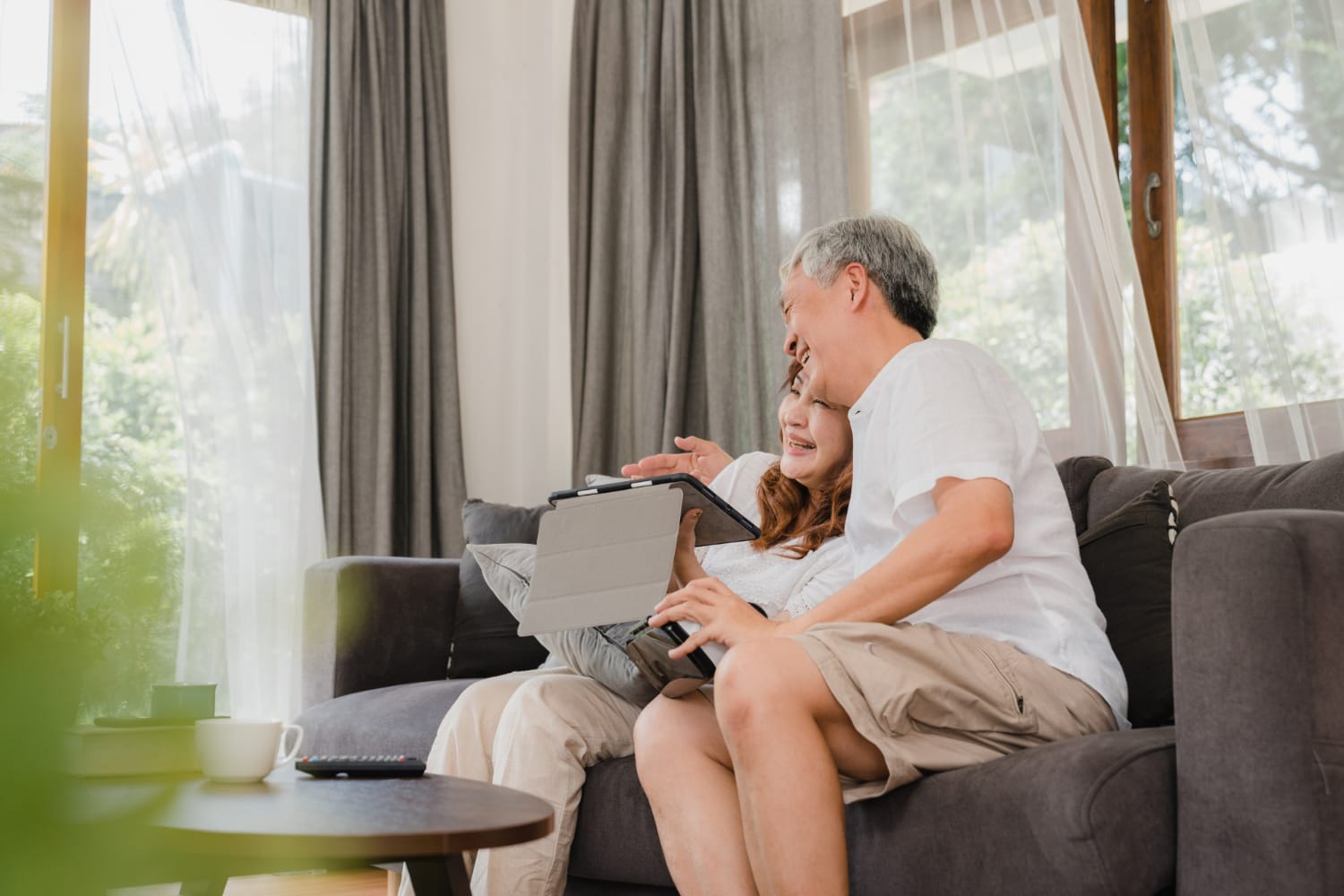 Asian elderly couple using tablet and virtual reality simulator playing games in living room, couple feeling happy using time together lying on sofa at home. Lifestyle senior family at home concept.