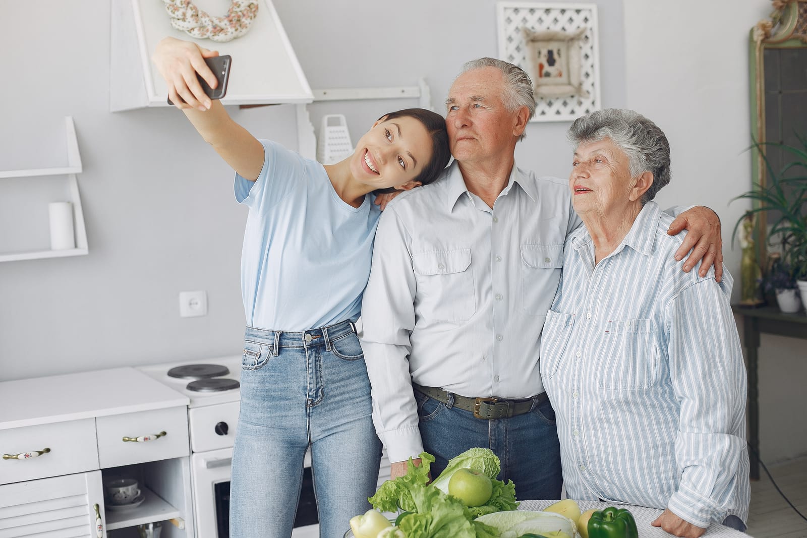 A young woman taking a selfie with her smiling grandparents in a bright kitchen