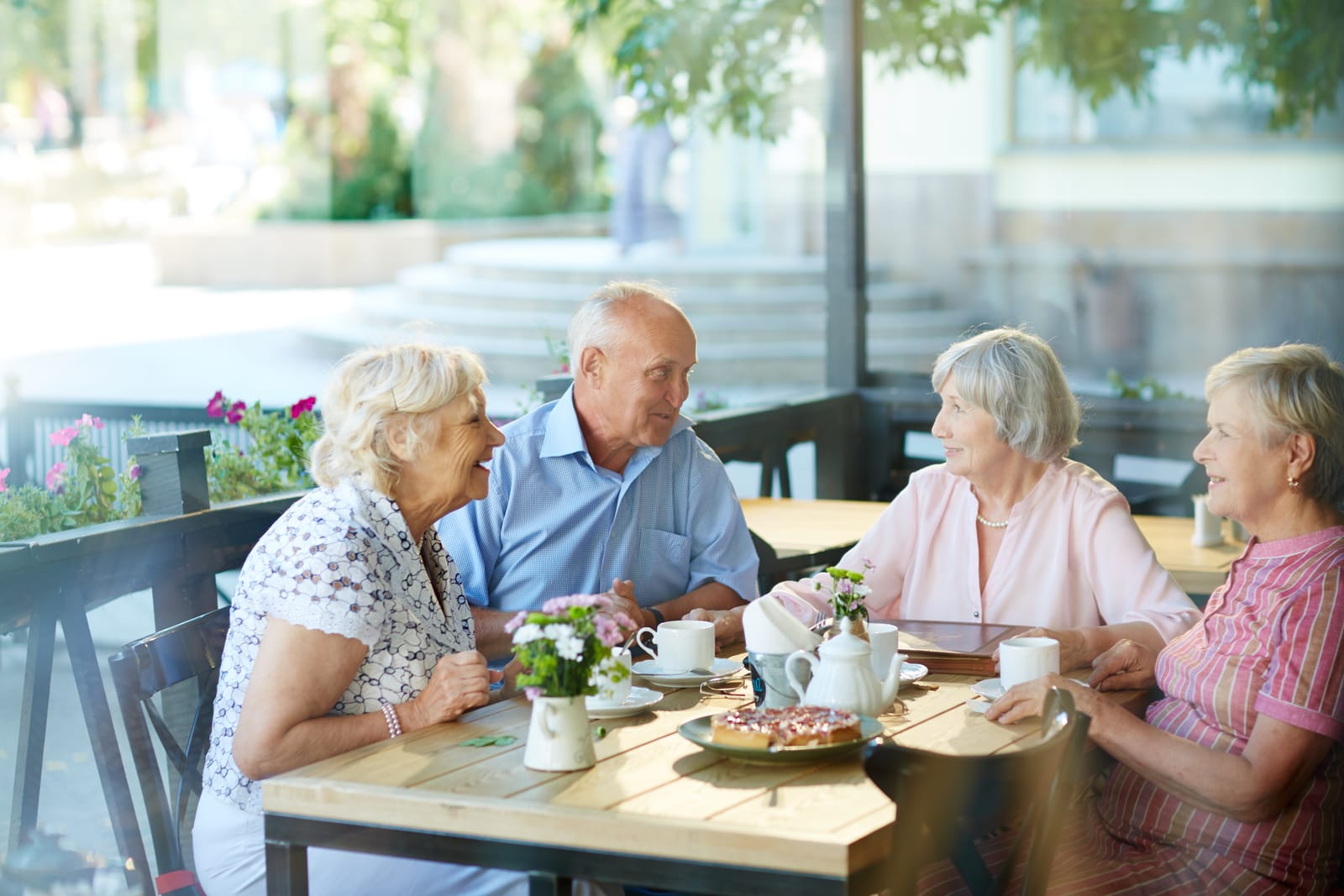 Four older friends laughing together over coffee and cake at an outdoor café